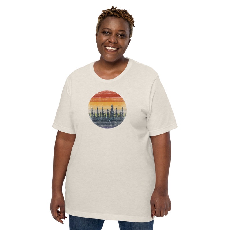 Puede incluir: Una camiseta blanca con un gr&aacute;fico de estilo vintage de una silueta de bosque contra un atardecer. El gr&aacute;fico est&aacute; en un c&iacute;rculo y presenta una combinaci&oacute;n de colores rojo, naranja, amarillo y azul.