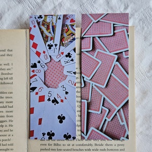 Könnte beinhalten: Zwei Lesezeichen mit einer Nahaufnahme eines Kartenspiels. Das erste Lesezeichen zeigt die Karten in einem Kreis angeordnet, wobei die Zahlen und Symbole sichtbar sind. Das zweite Lesezeichen zeigt einen Stapel Spielkarten, wobei die Rückseite der Karten zum Betrachter zeigt.