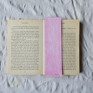 May include: A close-up of a book titled "The Hobbit" with a pink bookmark. The bookmark has the word "Khinh" written on it. The book is open to a page with text about a group of dwarves and a wizard named Gandalf.