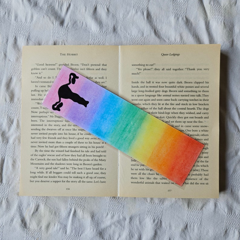 May include: A rainbow-colored bookmark with a black silhouette of a bird. The bookmark is made of watercolor paper and has a slightly textured surface.