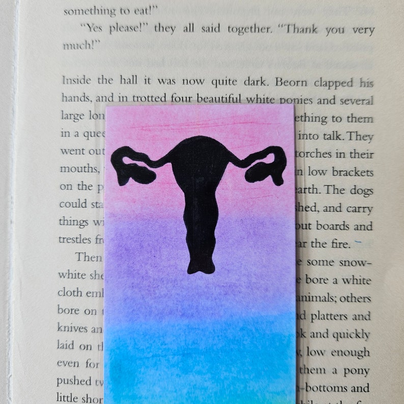 May include: A bookmark with a black silhouette of a female reproductive system on a pink, purple, and blue watercolor background.