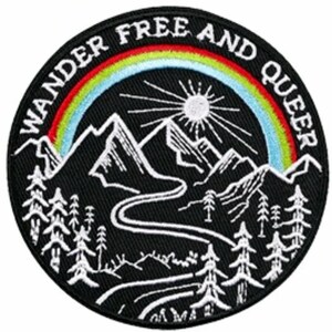 Könnte beinhalten: Schwarz-weiß gestickter Patch mit einem Regenbogenbogen über einem Gebirge und dem Text "Wander Free and Queer".