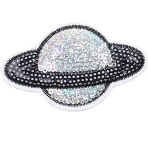 Könnte beinhalten: Ein weißer und schwarzer glitzernder Pailletten-Aufnäher mit einem Planeten mit einem Ring.