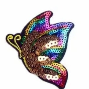 Könnte beinhalten: Ein bunter, schmetterlingsförmiger Pailletten-Patch mit braunem, schimmerndem und Regenbogen-Design. Der Patch ist perfekt, um Kleidung, Taschen oder anderen Accessoires einen Hauch von Glanz zu verleihen.