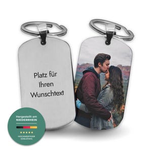 Könnte beinhalten: Zwei silberne Schlüsselanhänger in Form von Hundemarken. Einer zeigt ein Foto eines Paares, der andere den Text "Platz für Ihren Wunschtext". Die Schlüsselanhänger haben oben einen silbernen Ring. Ein grüner Kreis mit Text und Sternen befindet sich unten links.