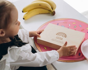 Könnte beinhalten: Eine Holzkiste mit einem Regenbogen-Design und dem Namen "Luzia" eingraviert. Die Kiste steht auf einem rosafarbenen und weißen Donut-förmigen Untersetzer.