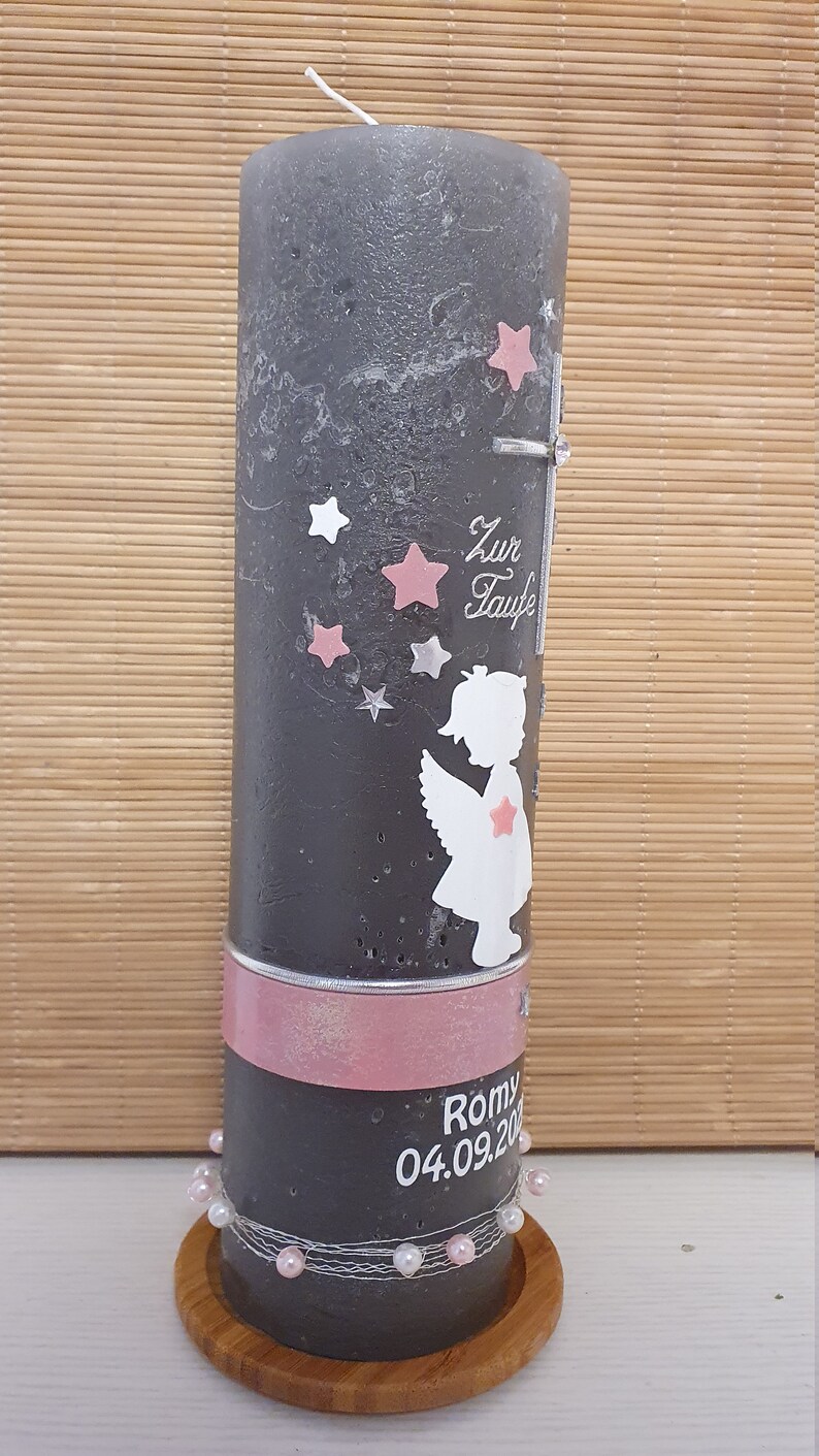 Pu&ograve; includere: Una candela grigia con un nastro rosa e dettagli di perle bianche. La candela ha una silhouette bianca di un angelo con stelle rosa e il testo "Zur Taufe" sul davanti. La candela &egrave; su una base di legno. Il testo "Romy 04.09.20" &egrave; sul fondo della candela.