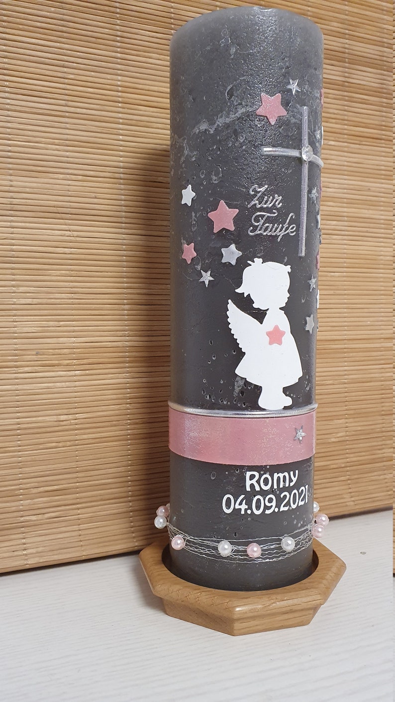 Pu&ograve; includere: Una candela battesimale grigia con un nastro rosa e perline bianche. La candela presenta una silhouette bianca di un angelo con stelle rosa e il testo "Zur Taufe" e "Romy 04.09.2021".