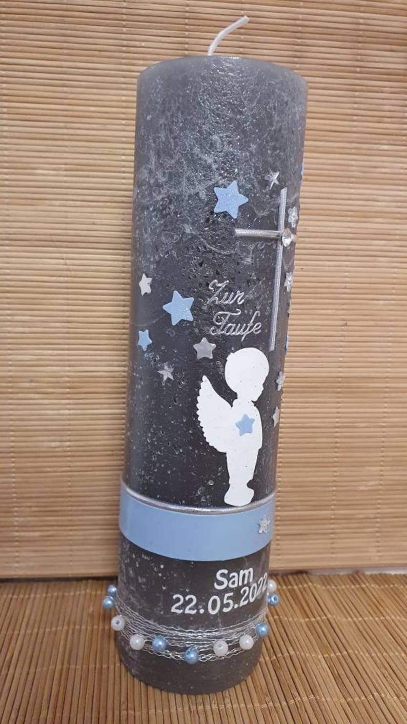 Pu&ograve; includere: Una candela battesimale grigia con un nastro blu e un design di angelo bianco. La candela ha il testo "Zur Taufe" e "Sam 22.05.2022" su di essa.