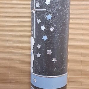 Pu&ograve; includere: Una candela grigia con un nastro blu e argento. La candela &egrave; decorata con stelle argentate e una silhouette bianca di un bambino. Il testo "Sam 5.2022" &egrave; stampato sulla candela.