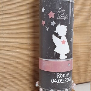 Pu&ograve; includere: Una candela battesimale grigia con un nastro rosa e perline bianche. La candela presenta una silhouette bianca di un angelo con stelle rosa e il testo "Zur Taufe" e "Romy 04.09.2021".