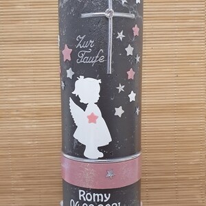 Pu&ograve; includere: Una candela battesimale grigia con un motivo a stelle rosa e bianche. La candela ha una croce argentata con un strass, una silhouette bianca di un angelo con ali rosa e il testo "Zur Taufe" in lettere argentate. La candela ha anche un nastro rosa con il nome "Romy" e la data "04.09.2021" in lettere bianche.