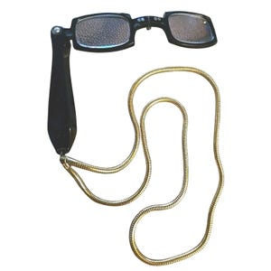 May include: Black folding reading glasses with rectangular lenses and a gold-colored chain. The glasses have a sleek, modern design, perfect for those who need reading assistance. The chain allows the glasses to be worn around the neck.