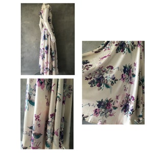 May include: A long white dress with a floral print in shades of purple and green. The dress has a fitted bodice and a flowing skirt.