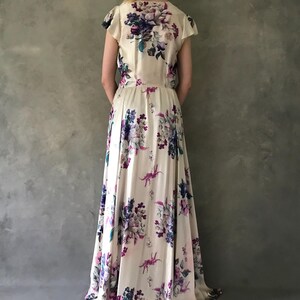 May include: A long, white maxi dress with a floral print featuring shades of purple, pink, and blue. The dress has a V-neckline and short sleeves.