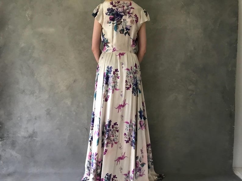May include: A long, white maxi dress with a floral print featuring shades of purple, pink, and blue. The dress has a V-neckline and short sleeves.