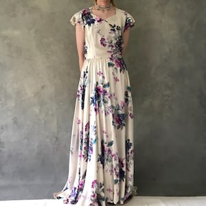 May include: A white maxi dress with a floral print featuring purple, blue, and green flowers. The dress has a scoop neckline and short sleeves.