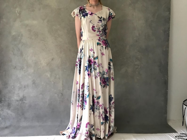 May include: A white maxi dress with a floral print featuring purple, blue, and green flowers. The dress has a scoop neckline and short sleeves.