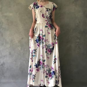 May include: A white maxi dress with a floral print in shades of purple, blue, and green. The dress has a fitted bodice and a flowing skirt.