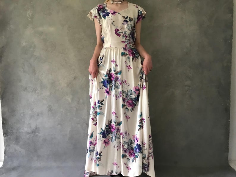 May include: A white maxi dress with a floral print in shades of purple, blue, and green. The dress has a fitted bodice and a flowing skirt.