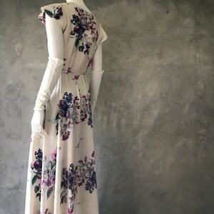 May include: A white maxi dress with a floral print featuring purple, pink, and green flowers. The dress has a fitted bodice and a flowing skirt.
