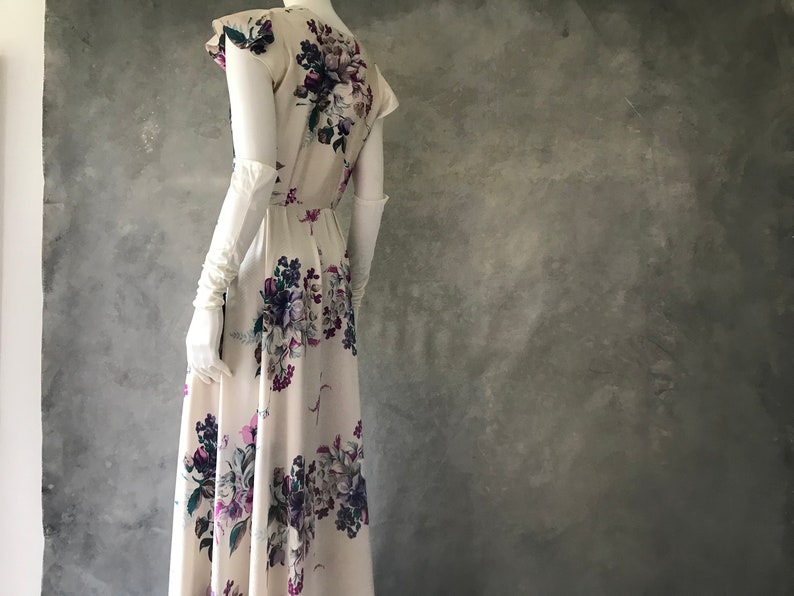 May include: A white maxi dress with a floral print featuring purple, pink, and green flowers. The dress has a fitted bodice and a flowing skirt.