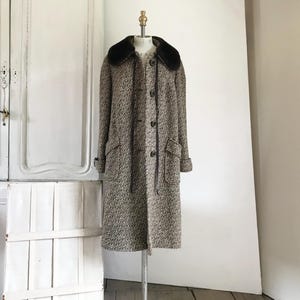 Puede incluir: Un abrigo vintage largo, con cuello de piel sintética negra. El abrigo tiene un estampado moteado marrón y blanco, con cierre de botones, dos bolsillos y mangas con puños. Se exhibe en un maniquí.