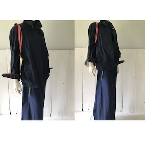 May include: A navy blue jacket with a red and white striped tote bag hanging from the shoulder. The jacket has a long, flowing skirt.