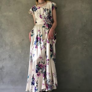 May include: A white maxi dress with a floral print featuring purple, blue, and green flowers. The dress has a scoop neck and short sleeves.