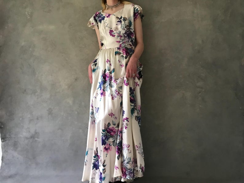 May include: A white maxi dress with a floral print featuring purple, blue, and green flowers. The dress has a scoop neck and short sleeves.