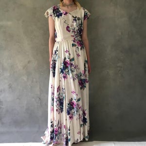 May include: A white maxi dress with a floral print in shades of purple, blue, and pink. The dress has a scoop neckline, short sleeves, and a fitted bodice. The skirt is full and flowing.