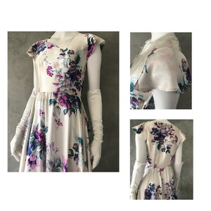 May include: A white satin dress with a floral print in shades of purple, teal, and pink. The dress has a V-neckline, short sleeves, and a full skirt. It is shown with white gloves.