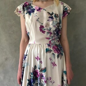 May include: A white dress with a floral print featuring purple, blue, and green flowers. The dress has a fitted bodice and a full skirt.