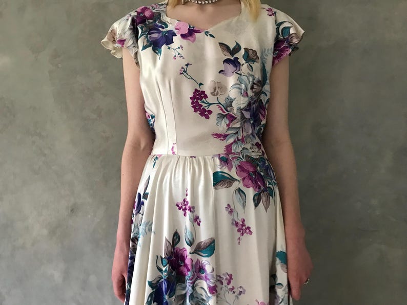 May include: A white dress with a floral print featuring purple, blue, and green flowers. The dress has a fitted bodice and a full skirt.