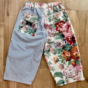 Puede incluir: Pantalones con diseño dividido, una pierna con rayas verticales azules y blancas y la otra con un estampado floral blanco con flores rojas, rosas y naranjas. Un bolsillo en el lado a rayas presenta una etiqueta de Lauren Ralph Lauren.