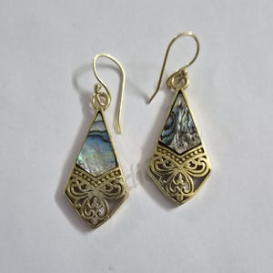 Peut inclure: Une paire de boucles d'oreilles pendantes dorées avec un motif en forme de cerf-volant. Chaque boucle présente une incrustation de nacre d'ormeau irisée sur le dessus et un motif en filigrane ajouré complexe en bas, suspendu par un crochet.