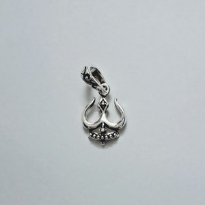 May include: A silver pendant in the shape of a stylized trident with a beaded design. The pendant has a loop at the top for attaching to a chain.