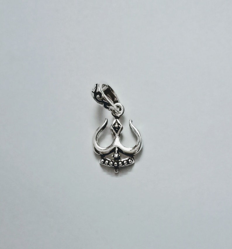 May include: A silver pendant in the shape of a stylized trident with a beaded design. The pendant has a loop at the top for attaching to a chain.