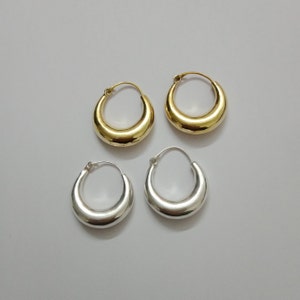 May include: A pair of gold and silver hoop earrings. The earrings are both round and have a slightly curved shape.