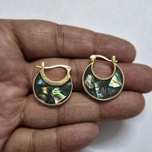 Könnte beinhalten: Ein Paar kleine goldfarbene Creolen mit einer halbmondförmigen Einlage aus schillernden Abalone-Muschelfragmenten. Die Muschelstücke zeigen verschiedene Farben wie Grün, Rosa und Blau und sind in einen glatten, polierten Metallrahmen gefasst.