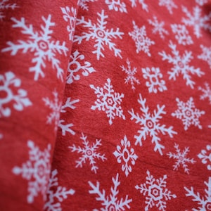 Könnte beinhalten: Roter Stoff mit einem weißen Schneeflockenmuster. Der Stoff ist in der Mitte gefaltet, sodass das Muster auf beiden Seiten sichtbar ist.