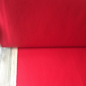 Könnte beinhalten: Eine Rolle leuchtend roten Stoffes. Der Stoff ist glatt und hat einen leichten Glanz.