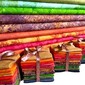 Könnte beinhalten: Ein Stapel bunter Stoffquadrate, die mit einem Band zusammengebunden sind und in einem Regenbogenmuster angeordnet sind. Der Stoff ist eine Mischung aus Texturen und Mustern, darunter Paisley, Blumen und Batik.