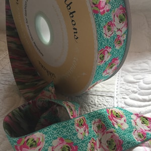 Könnte beinhalten: Eine Rolle türkisfarbenes Band mit einem Blumenmuster mit rosa und weißen Rosen. Das Band befindet sich auf einer Spule mit dem aufgedruckten Text "Exclusive Ribbons for fashion and design" und "www.FairisleRibbons.com".