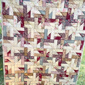 Könnte beinhalten: Eine Patchwork-Decke mit einem geometrischen Muster in Beige-, Braun-, Rot- und Blautönen. Die Decke besteht aus verschiedenen Blumenstoffen und hängt an einer Wäscheleine.