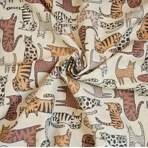 Könnte beinhalten: Ein beigefarbener Stoff mit einem sich wiederholenden Muster aus braunen und schwarzen Katzen. Die Katzen sind in einer einfachen, stilisierten Art und Weise gezeichnet und schauen in verschiedene Richtungen. Der Stoff ist perfekt für Bastelprojekte, wie zum Beispiel das Nähen von Taschen, Kissen oder Decken.