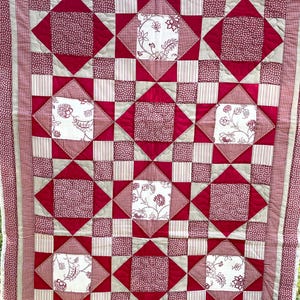 Könnte beinhalten: Eine rot-weiße Patchwork-Decke mit einem Sternenmuster. Die Decke besteht aus verschiedenen Stoffen mit verschiedenen Mustern, darunter Gingham, Punkte und Blumenmuster.