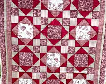 Könnte beinhalten: Eine rot-weiße Patchwork-Decke mit einem Sternenmuster. Die Decke besteht aus verschiedenen Stoffen mit verschiedenen Mustern, darunter Gingham, Punkte und Blumenmuster.