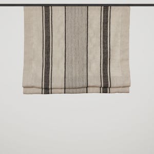May include: Beige linen window blind with vertical dark grey stripes. The blind hangs from a black rod. The central stripe features thin, closely spaced lines, while the outer stripes are wider.