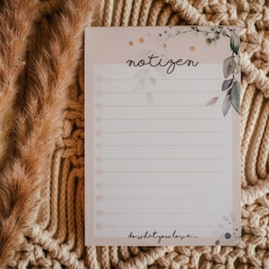 Könnte beinhalten: Ein Notizblock mit dem Wort "notizen" in Schrift, floralen Akzenten und linierten Seiten mit herzförmigen Aufzählungszeichen. Der Satz "do what you love" steht unten. Der Notizblock befindet sich auf einem Makramee-Hintergrund mit getrockneten Pflanzen.